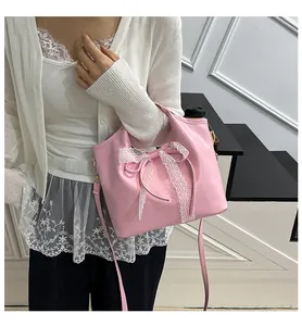 Detail view of pink leather handbag featuring a delicate white lace bow and strap