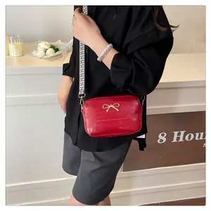 Close-up of red crossbody bag with golden bow detail and woven geometric strap