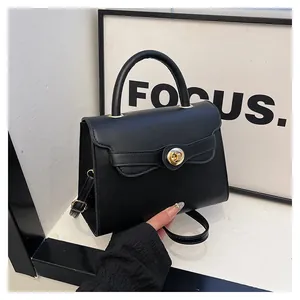 Detail of black matte handbag featuring a gold circular twist lock and sleek handle