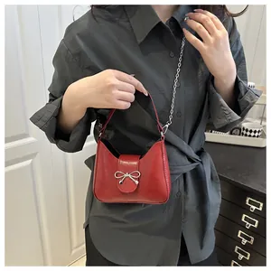 Détail d'un sac sous le bras rouge brillant avec noeud argenté et bandoulière chaîne