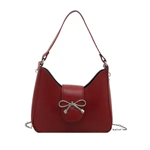 Sac sous le bras en cuir rouge élégant avec nœud argenté et bandoulière sur fond blanc