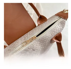 Close-up of golden metal zipper and woven leather texture on cream commuter handbag