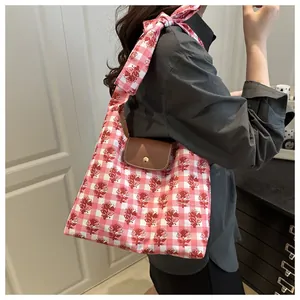 Pink plaid tote bag with floral prints and brown leather flap shown on a shoulder