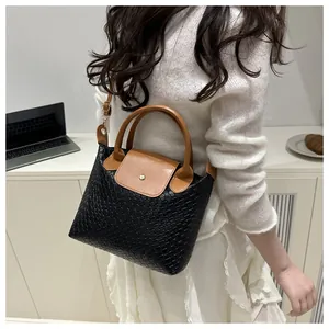 Close-up of black woven texture leather handbag with brown handles and gold clasp