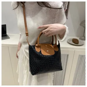 Detail of black woven texture bag with brown leather handles and gold metal hardware