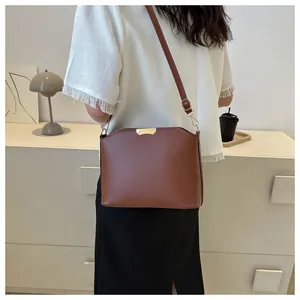 Detail of vintage brown leather crossbody bag with gold metal accents on model