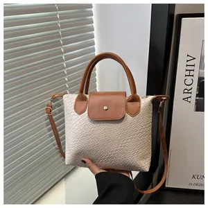 Detail of woven texture handbag with brown leather flap and adjustable shoulder strap