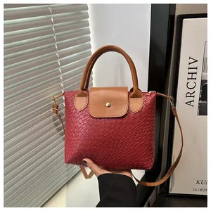 Detail of red woven texture handbag with brown leather handle and gold metal clasp lock