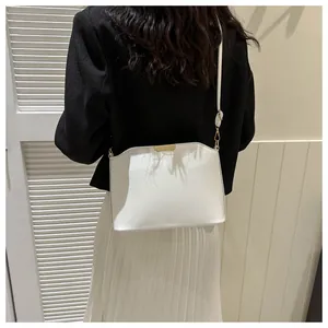 Detailed view of the white minimalist shell bag with gold hardware worn by a model