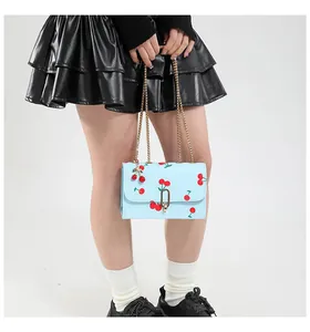 Detail of light blue cherry print saddle bag with gold chain and cherry charm accessory