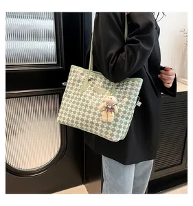 Detail showing green checkered tote bag with plush bear charm and metallic logo plate