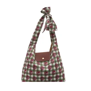 Floral print green plaid tote bag with brown flap and bow shoulder strap on white base