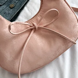 Detailopname van een roze halvemaantas met een fijn strikje en vintage matte textuur