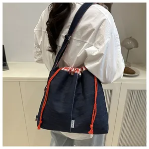 Detail of blue denim crossbody bag featuring orange drawstring and red checkered lining