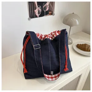 Close-up of denim drawstring bucket bag with red checkered lining and adjustable strap