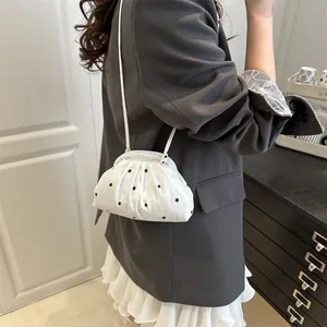 Witte geplooide crossbodytas met bloemenprint gedragen door een model binnenshuis
