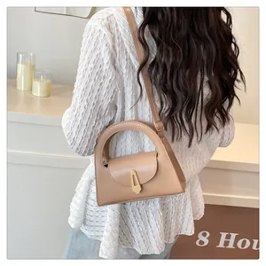Detail of khaki semicircular handbag showing metal lock and arched handle on model