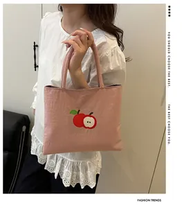 Détail de la broderie pomme sur un sac cabas rose en nylon tenu par un mannequin chic