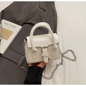 Detail of white mini handbag with metal buckle and silver chain strap on grey blazer
