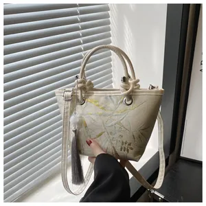 Detailed view of floral embroidery on a white tote bag with elegant tassel and handles