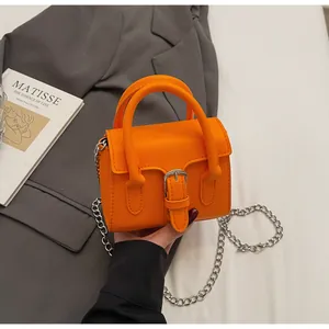 Macro detail of bright orange PU leather handbag with silver buckle and chain strap