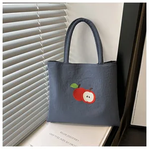 Gros plan de la broderie pomme sur le sac fourre-tout en nylon bleu morandi poli