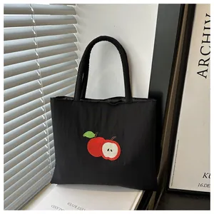 Détail de la broderie de pomme rouge sur un sac cabas en nylon noir à texture fine