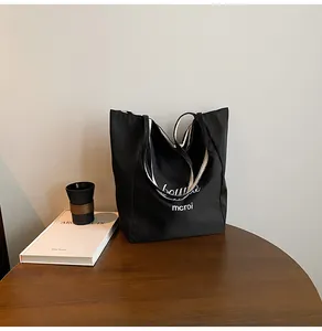 Détail du sac cabas noir avec poignées rayées et lettrage blanc sur une table en bois