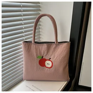 Gros plan sur un sac cabas en nylon rose avec broderie détaillée de pommes rouges
