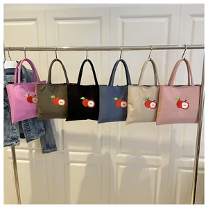 Détail de six sacs en nylon colorés avec broderie de pomme rouge suspendus au portant