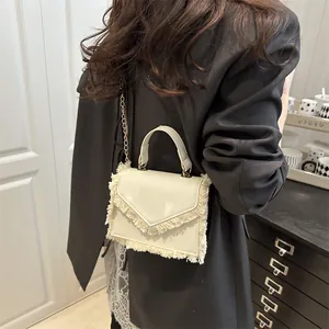 Cremeweiße PU-Leder Handtasche mit Fransenbesatz und goldener Kette an einem Model
