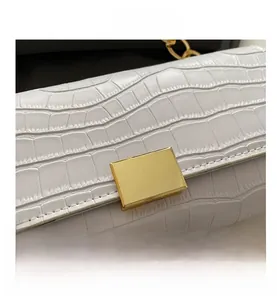Detail shot of white crocodile embossed leather bag featuring a gold metal buckle