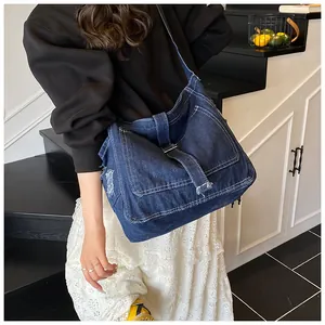 Detail of dark blue denim messenger bag with white contrast stitching and vintage metal buckle