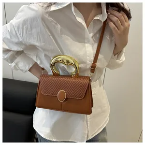 Close-up of brown leather bag with woven flap and artistic golden metal handle