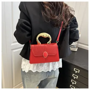 Detail of red textured crossbody bag with gold sculptural metal handle and patchwork design