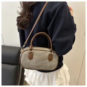 Detail of grey denim bowling bag featuring brown leather handles and gold metal hardware