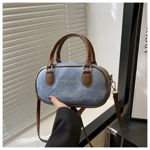 Detail of light blue denim bowling bag with brown leather trim and golden logo