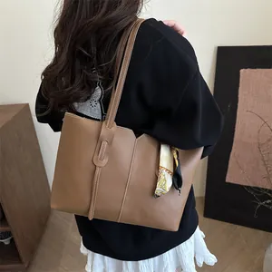 Brown leather tote bag with contrast stitching and decorative scarf on shoulder