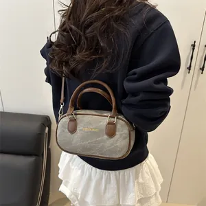 Mini gray denim bowling bag with brown leather trim shown as a crossbody on model