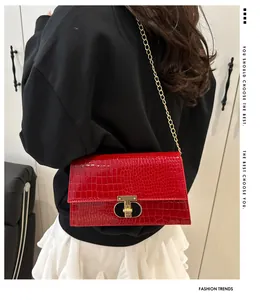 Detailopname van rode tas met krokodillenprint en gouden T-vormige metalen sluiting