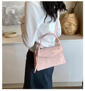 Detail of pink glossy handbag with knot handle and gold hardware on model