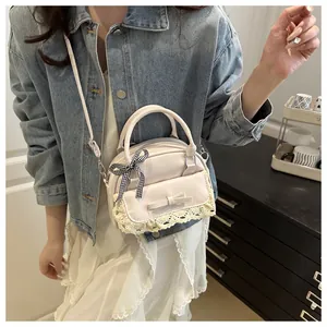 Détail du sac crème avec bordure en dentelle, nœud en cuir et ruban à carreaux noir