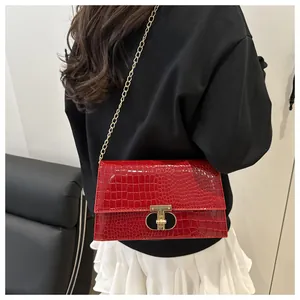 Detail van rode handtas met krokodillenmotief, gouden T-sluiting en kettingriem