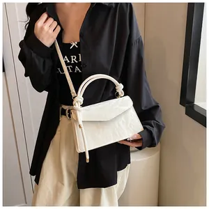 Close-up of white glossy crossbody bag with knot handle worn by model in soft light