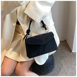 Detail of black pleated faux leather handbag with braided handle held by model