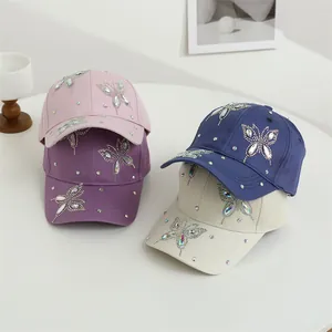 Dettaglio di quattro cappellini da baseball con motivi a farfalla in strass luccicanti su vari colori