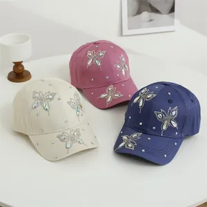 Dettaglio di tre berretti da baseball con motivi a farfalla in strass di vari colori