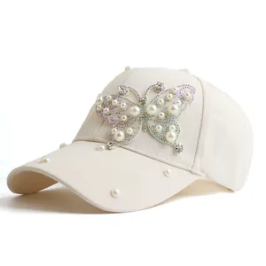 Close-up of artificial pearls and rhinestones butterfly detail on cream baseball cap