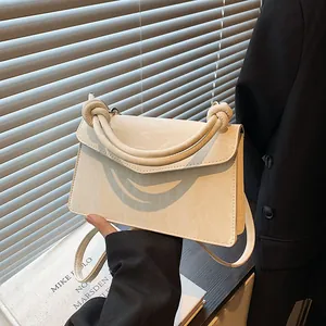 Elegant cream square handbag with knotted handles and V-shaped flap on office background