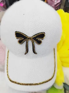 Close-up of plush white baseball cap featuring black bow and golden bead chain detail